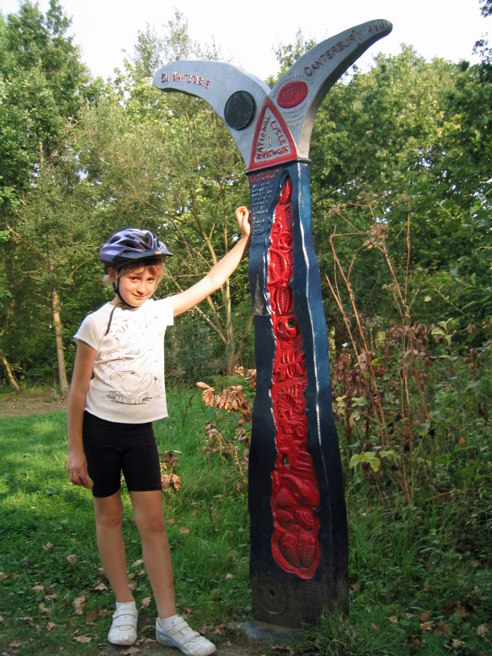 Miss Three Points of the Compass dwarfed by Sustrans Milestone on Crab and Winkle cycleway