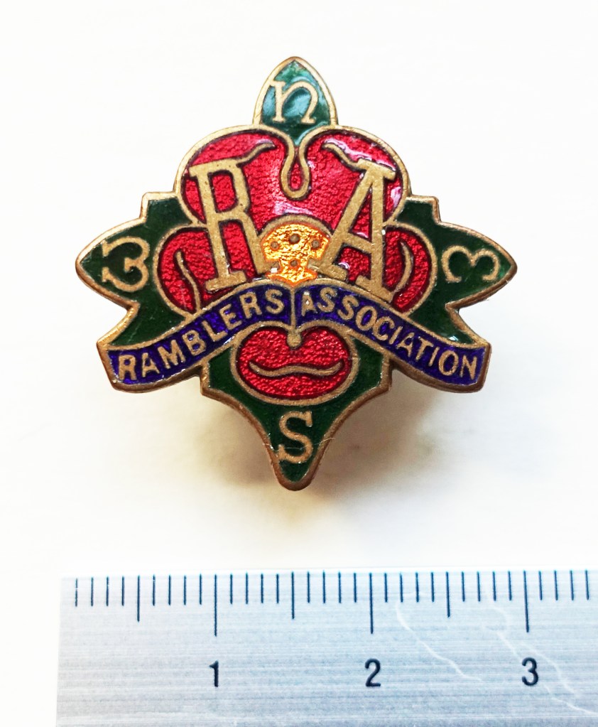 Ramblers Association badge. 1930's - 1950's. Compass Rose, the first logo for the Ramblers Association. Made from enamelled metal, it shows red petals against green leaves on which the four cardinal points of the compass appear. These and the words Ramblers Association, with it's initials above, are gilded.
