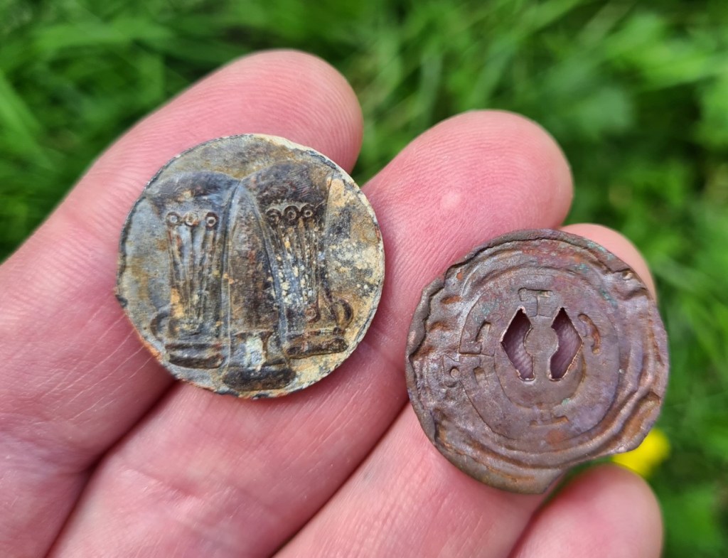 Back and front of original lead and copper waymerks. There is some calcification and age related patination to both of these. Designs show Bronze Age trade axes on left and Edin's Hall Broch on right. The copper waymerk also has a Scottish 'thistle logo', punched through it. This is now Scotland’s Great Trails branding